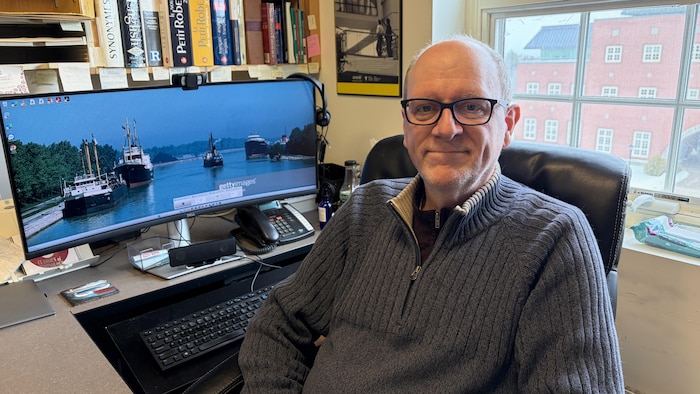 Un homme assis à son bureau sourit à la caméra.