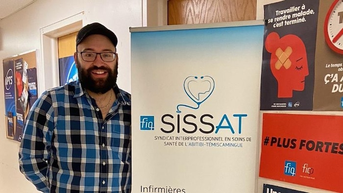 Jean-Sébastien Blais pose à côté d'une affiche de la FIQ-SISSAT.