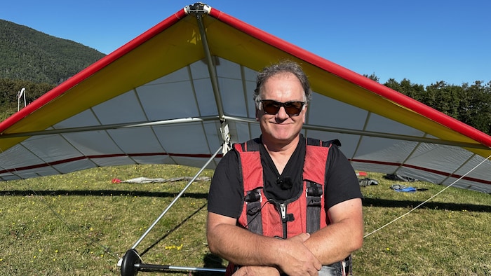 Jean-Sébastien Cloutier, en combinaison de deltaplane devant son appareil, croise les bras avec des lunettes de soleil.