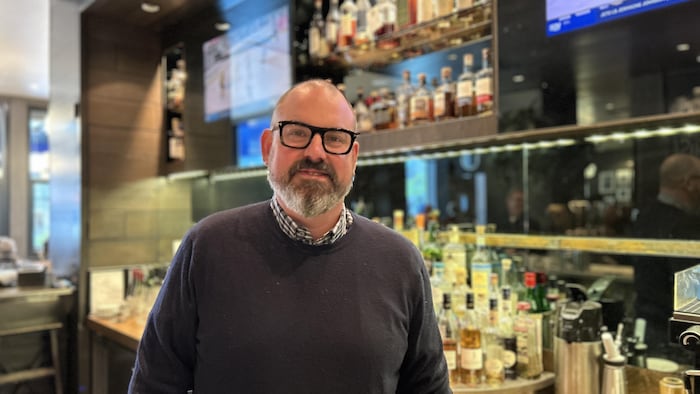Portrait du gérant devant le comptoir du bar d'un restaurant.