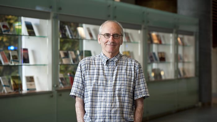 Jean Thomas Bernard pose dans un couloir en avant d’une bibliothèque.