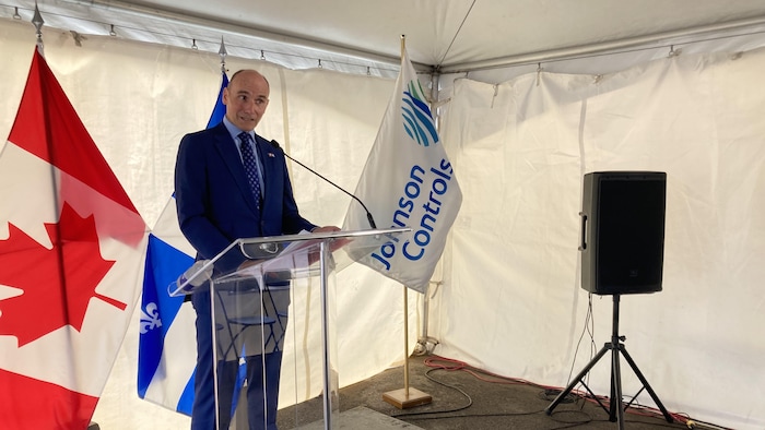 Jean-Yves Duclos prononce une allocution sous un chapiteau blanc. Il se tient debout, derrière un lutrin et devant des drapeaux du Canada, du Québec et de l'entreprise Johnson Controls.