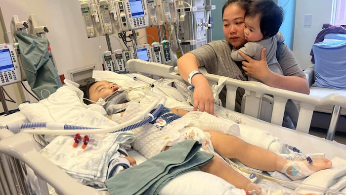 Un enfant dans un lit d'hôpital, accompagné de sa mère et de sa petite sœur.