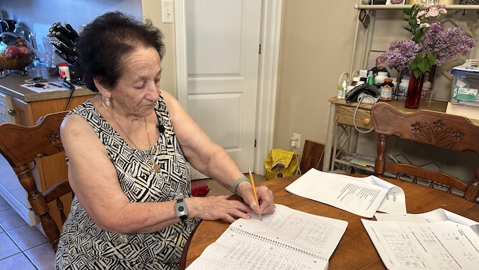 Jeannette Cormier est assise à la table à manger. Elle écrit au crayon dans un cahier.