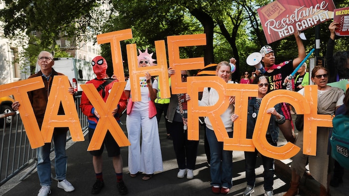 Demonstrators hold up signs and large letters that together spell “tax the rich”.