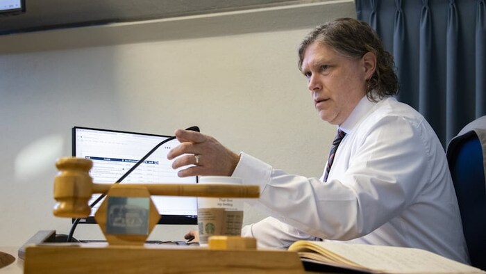 Jeff Fawcett, assis à son bureau durant une rencontre, prend la parole et pointe une personne du doigt.
