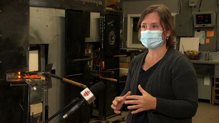 Une souffleuse de verre, masque sur le visage, donne des explications dans l'atelier de la coopérative.