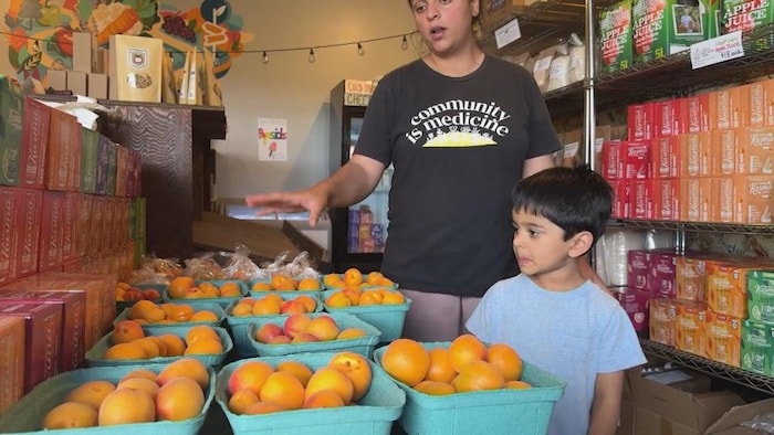 Une femme et un petit garçon dans une épicerie devant des barquettes de prunes.