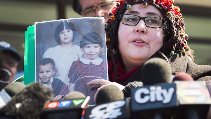 Une femme tient la photo de trois enfants devant les micros de journalistes.