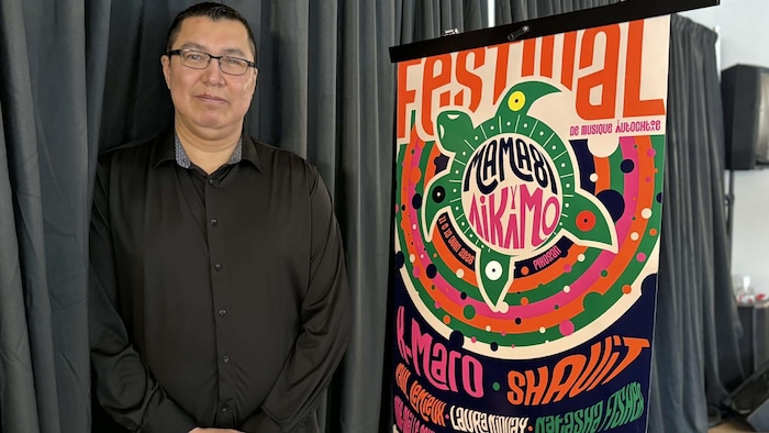 Jeremy Kistabish est debout devant une affiche de festival. 