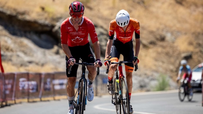 Deux cyclistes, debout sur leurs pédales, montent une côte durant une course. Jérôme Gauthier sourit durant l'effort.