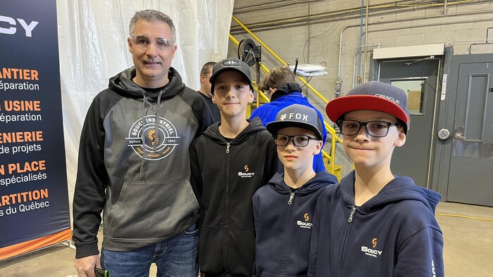 Un homme avec un chandail Soucy Indusrtiel est accompagné de ses trois fils.
