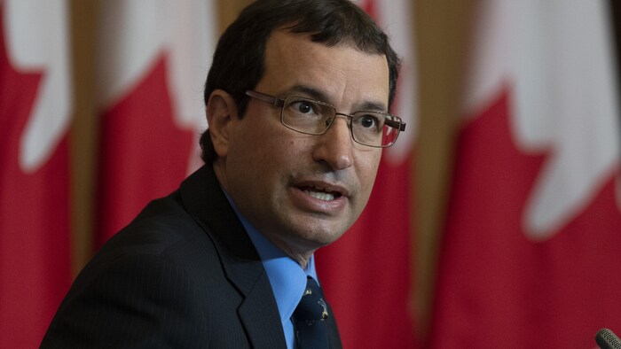 Jerry DeMarco parle devant des drapeaux canadiens. 