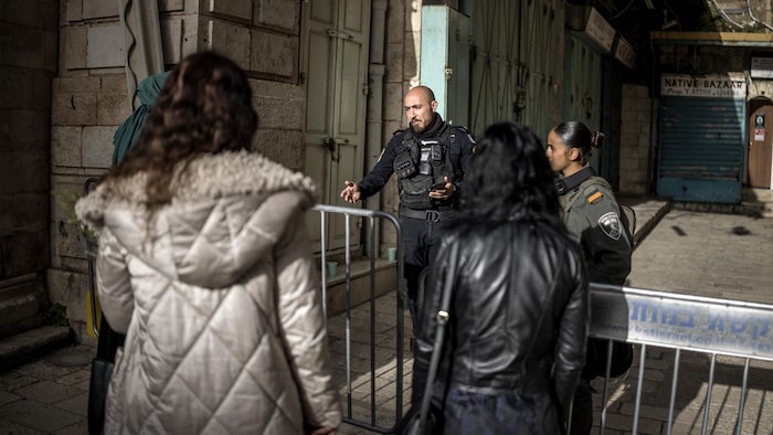 Derrière une barrière de sécurité, un policier israélien explique à un groupe de pèlerins chrétiens orthodoxes qu'ils ne sont pas autorisés à entrer dans l'église du Saint-Sépulcre, où doit être célébrée la messe du dimanche de Pâques à huis clos, le 5 avril 2026. 