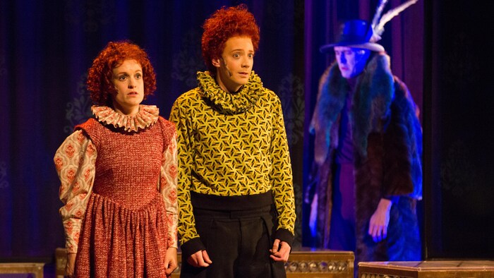 Sur une scène, trois acteurs vêtus de costume d’époque.