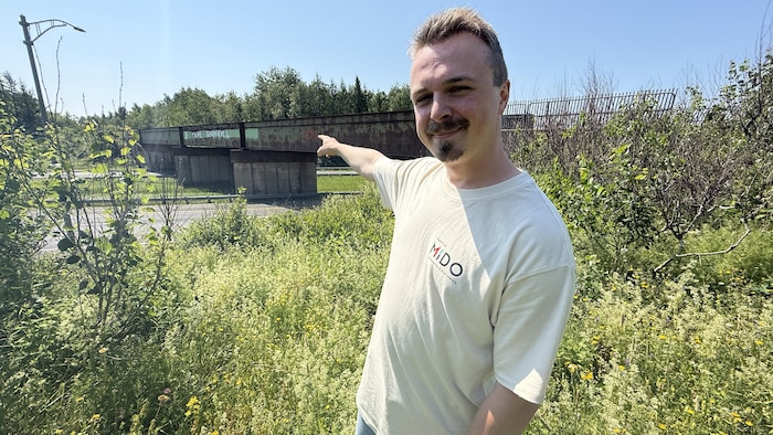 Un homme pointe le pont ferroviaire sur le quel se trouve le graffiti.