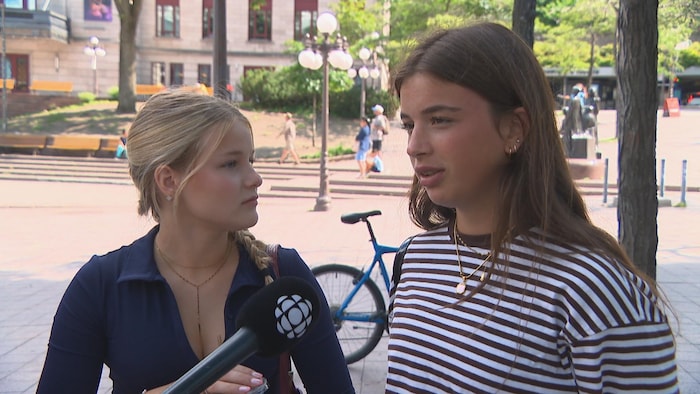 Une jeune fille parle devant un micro de Radio-Canada en compagnie d'une amie qui se tient à ses côtés.
