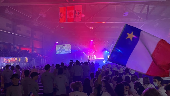 Un drapeau acadien flotte au-dessus d'une foule dans un aréna.