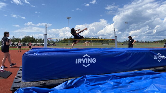 Un adolescent est dans les airs et passe par-dessus la barre à l'épreuve du saut en hauteur..
