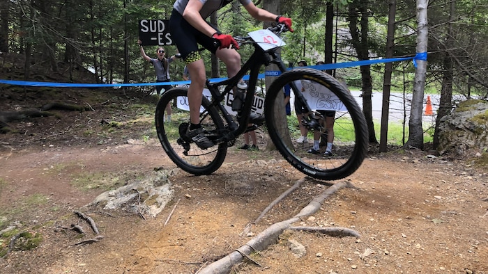 Un adolescent sur sa monture négocie des obstacles d'une épreuve de vélo de montagne. On voit derrière des gens qui lèvent des pancartes sur lesquelles ils ont écrit les mots « Sud-Est ».