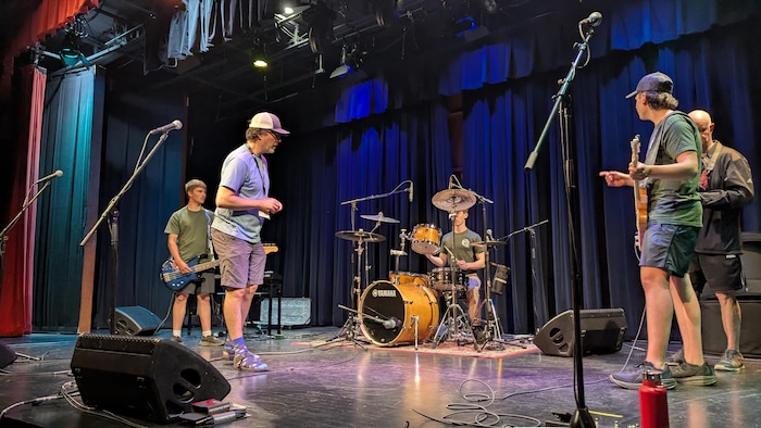 Instructeur sur scène avec trois jeunes musiciens. 