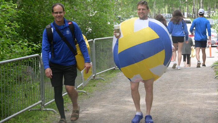 Un homme habillé d'un costume gonflable de ballon de volleyball tenant un café. 