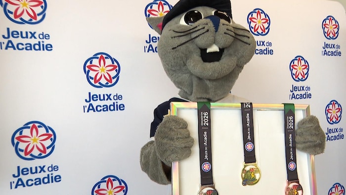 Une personne portant un costume de lièvre tient des exemples des médailles de bronze, argent et or.