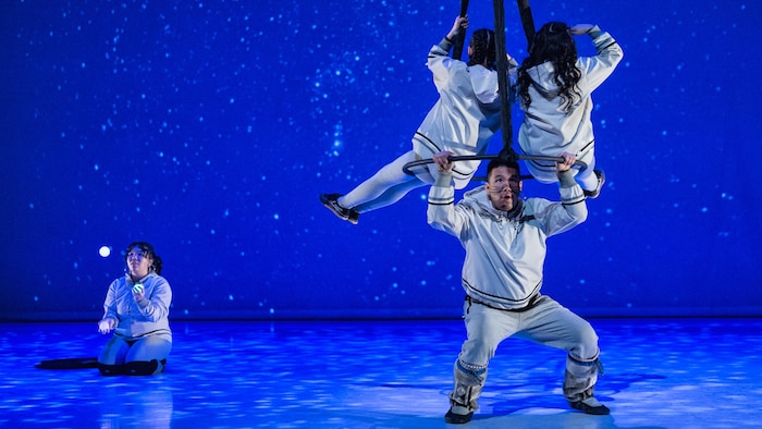 Une jeune jongle avec des balles lumineuses tandis que trois autres font des acrobaties dans les airs.