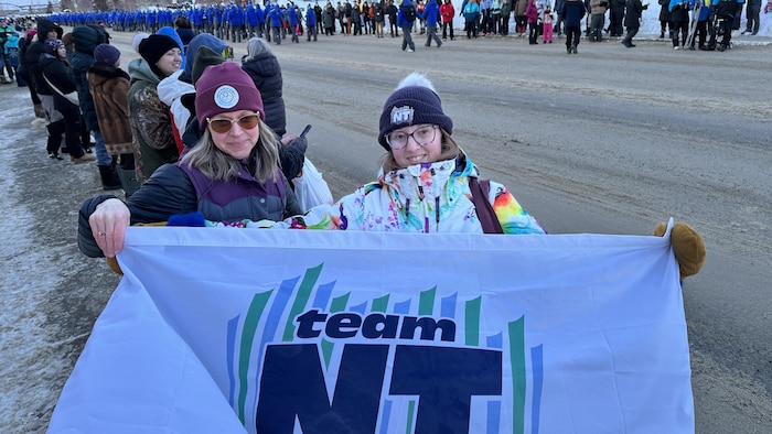 Deux femmes tiennent un drapeau sur lequel on peut lire "Team NT" dans une foule.