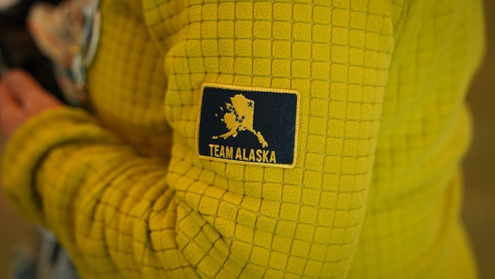 Un jeune, dont on ne voit pas le visage, porte un chandail jaune avec un écusson sur lequel se lit "Team Alaska".