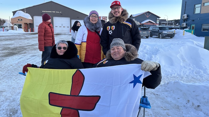 Mona et George Okalik, assis sur des chaises, tiennent un drapeau du Nunavut et deux autres sont debout derrière elles.