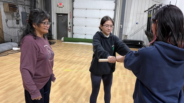Lorna Storr observe Tthën Catholique et Brooke-Lyn Bodnar, qui tiennent un bâton tendu entre elles.