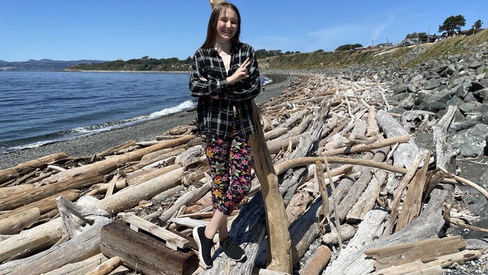 Une jeune devant une construction faite de bois flottant, au bord de l'eau