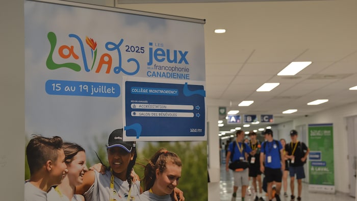 Des jeunes marchent devant une affiche promouvant les Jeux de la francophonie canadienne.