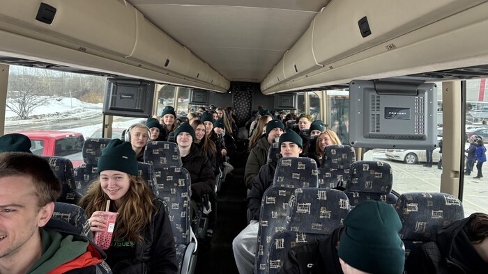 Des jeunes assis dans un autobus sourient.