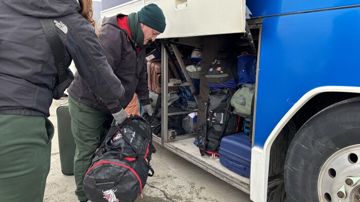 Un homme place des bagages dans le compartiment sous un autobus.