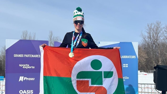 Zoé Lacroix pose sur le podium avec le drapeau de la délégation de l'Abitibi-Témiscamingue et une médaille d'or au cou.