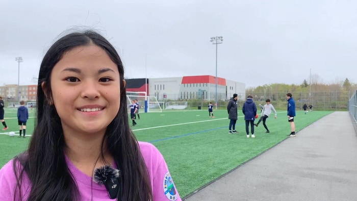 Une adolescente sourit pendant qu'elle est debout sur les lignes de côté d'un terrain de football synthétique extérieur.