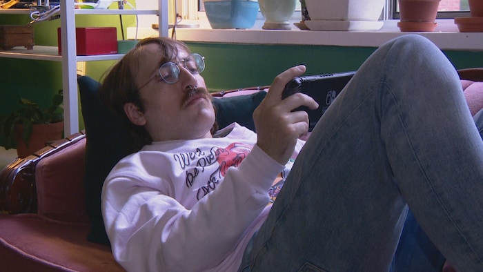 Un homme étendu sur un divan joue à un jeu vidéo. 