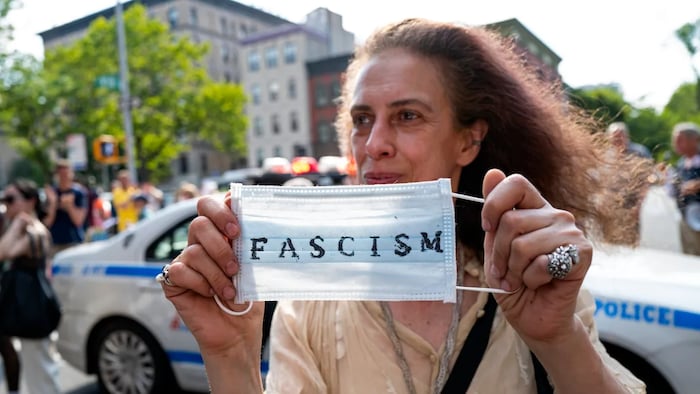 An activist holds up a surgical mask during a protest of a visit by First Lady Jill Biden and Dr. Anthony Fauci at a COVID-19 vaccine clinic in Harlem, N.Y., in June 2021.