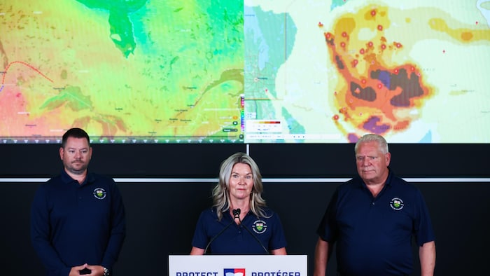 La ministre de la Préparation aux situations d’urgence, Jill Dunlop, entourée de Mike Harris (à gauche), et du premier ministre de l’Ontario, Doug Ford (à droite), se tient devant une carte en temps réel du déplacement de la fumée lors d’une conférence de presse visant à faire le point sur les feux de forêt en cours en Ontario, à Toronto, le vendredi 17 juillet 2026.