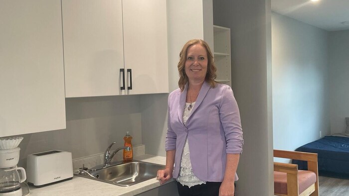 Jill Green pose debout à côté de l'évier de la cuisine d'un appartement inhabité.