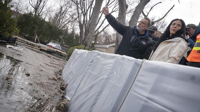 Deux personnes sont debout derrière une barrière modulaire qui bloque de l'eau.






