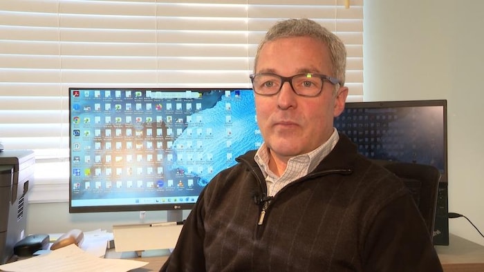 Jim Cormier est assis à son bureau avec un ordinateur en arrière plan.