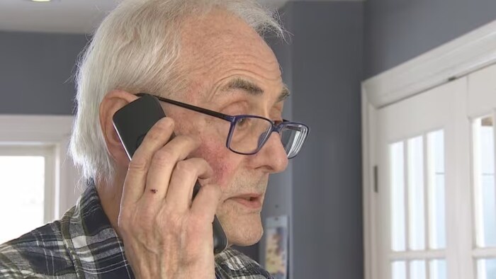 Un vieil homme tient un téléphone à son oreille.