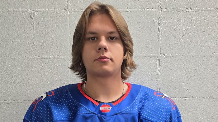 Un jeune homme portant le chandail de hockey des Mustangs pose pour une photo officielle.