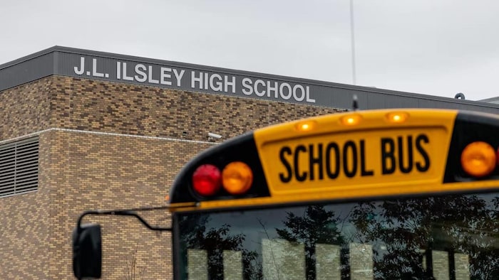 Un autobus scolaire devant une école dont le nom apparaît en grosses lettres blanches sur la façade.