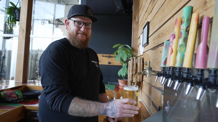 Un homme fait couler de la bière en fût dans un verre derrière un bar.