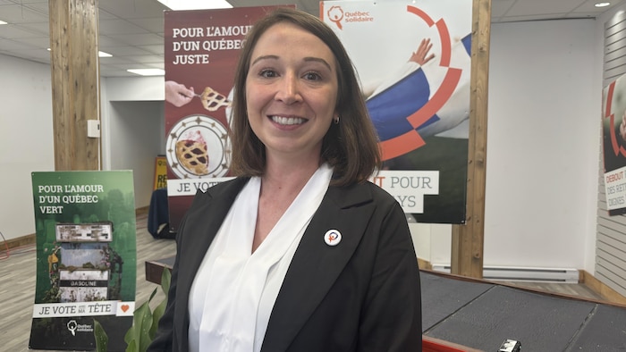 Joanie Bolduc sourit à la caméra devant des affiches électorales de Québec solidaire dans une salle.