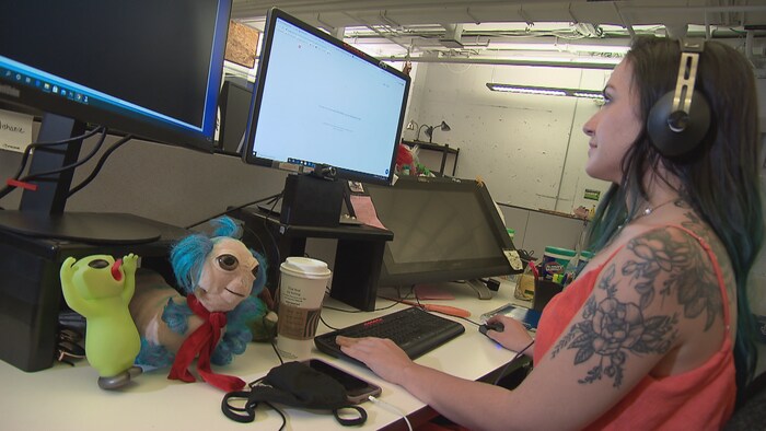 Jeune femme tatouée en camisole fixe un écran d'ordinateur avec des écouteurs sur la tête